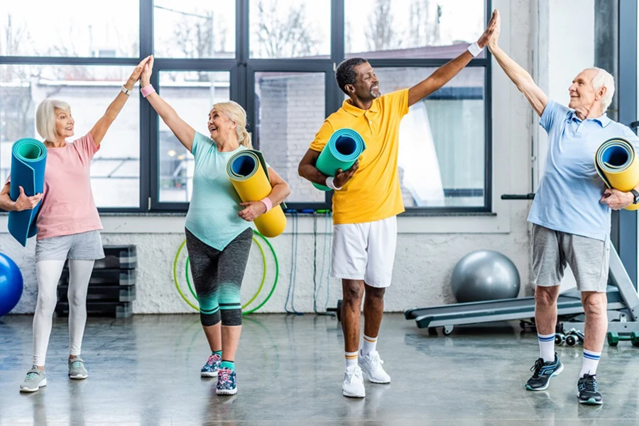 laughing senior multiethnic athletes with fitness mats taking high fives to each other at gym